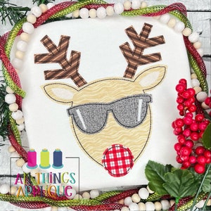 May include: Embroidered applique design of a reindeer wearing sunglasses and a red and white checkered nose. The reindeer is brown and white with a striped pattern on its antlers.