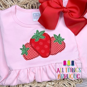 Op de afbeelding: Roze longsleeve shirt met een gerimpelde zoom en een aardbei-applicatie. De applicatie is gemaakt van rode stof met witte stippen en groene bladeren.