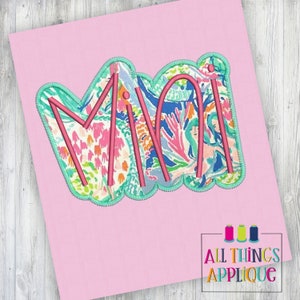 May include: A pink fabric applique with the word "MIA" in a white and pink floral pattern. The letters are outlined in teal.