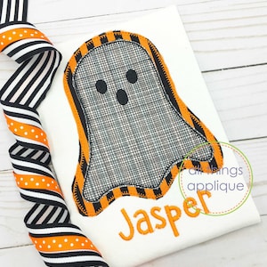 May include: A white fabric with an orange and black striped ghost applique. The ghost has a black mesh design and a black face with two eyes and a mouth. The name "Jasper" is embroidered in orange below the ghost.