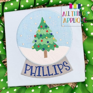 May include: A blue and white snow globe with a green Christmas tree inside. The snow globe has a checkered base and the name "PHILLIPS" is embroidered below it.