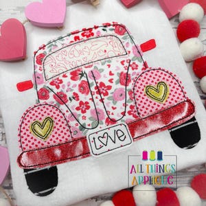 May include: An embroidered Valentine's Day themed car applique. The car features a floral pattern with red and pink roses, hearts, and the word "Love". Gold heart accents are on the car's sides. The design is set against a white background.