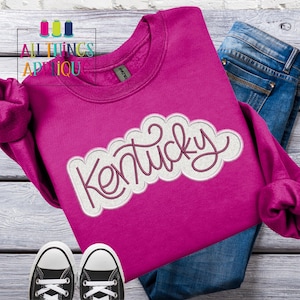 Puede incluir: Una sudadera rosa con un dise&ntilde;o bordado en blanco y rosa que dice "Kentucky".