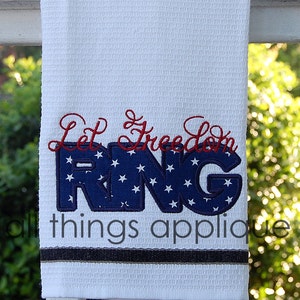 Op de afbeelding: Witte keukendoek met de tekst "Let Freedom Ring" geborduurd in rood en blauw. De letters zijn versierd met witte sterren op een blauwe achtergrond.