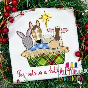 May include: A white shirt with an embroidered image of the nativity scene. The scene includes a baby Jesus, a donkey, a cow, and a sheep. The text "For unto us a child is born" is embroidered below the scene.