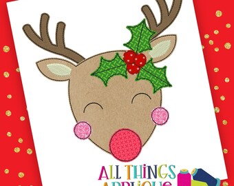 May include: A cute cartoon reindeer face with a red nose, pink cheeks, and a green holly sprig on its head. The reindeer is smiling with its eyes closed. The image is a digital embroidery design.