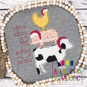 May include: A gray sweatshirt with a red embroidered name "Rhi Rhi" and a stack of three animals wearing Santa hats. The animals are a chicken, a pig, and a cow. The text "All Things Applique" is embroidered in the bottom right corner.