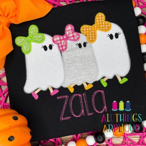 May include: Three white ghosts with different colored bows on their heads. The ghosts are wearing shoes and have a name "Zala" stitched below them. The image is on a black background.
