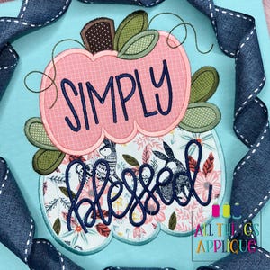 May include: A pink and green applique design of a pumpkin with the words "Simply Blessed" in a blue script font.