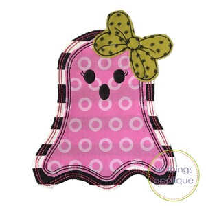 May include: Pink ghost with a black and white striped border and a green bow. The ghost has a white polka dot pattern and a black face with eyelashes and a mouth.
