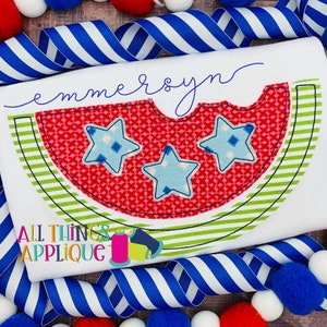 May include: A white t-shirt with a red and green watermelon design. The watermelon has three blue stars inside. The text "emmersyn" is written in cursive above the watermelon. The text "All Things Applique" is written in the bottom left corner of the shirt.