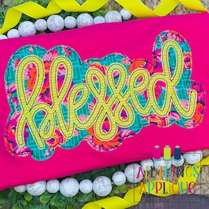May include: A pink fabric with a yellow and green floral applique that says "Blessed" in a yellow script font.