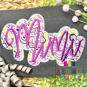 May include: A gray shirt with a pink and green floral applique of the name "Mimi" in a cursive font. The applique is outlined in white and has a stitched edge.