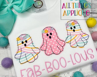 May include: White t-shirt with three ghost appliqués, each adorned with a floral crown. The ghosts have striped and polka-dot patterns in pastel colors. The text "FaB-BOO-LOUS" is embroidered in pink. A large teal bow is visible.