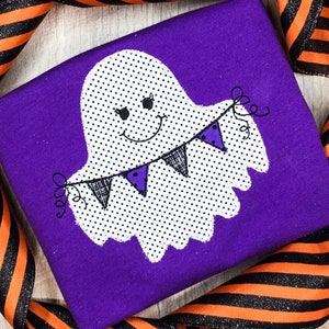 May include: A purple fabric with a white ghost holding a string of black and purple pennants. The ghost has black eyes and a smiling mouth. The ghost is covered in white polka dots.