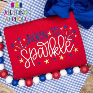 May include: Red t-shirt with white and blue embroidery that says "Born to Sparkle" with gold and blue stars and fireworks.