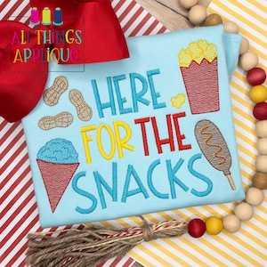 May include: A light blue t-shirt with the text "Here for the Snacks" in blue, red, and yellow embroidery. The design also includes embroidered images of peanuts, popcorn, a snow cone, and a corn dog.