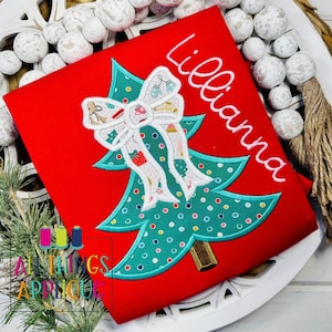 May include: Red Christmas shirt with a green and white embroidered Christmas tree with a white bow and the name "Lilliana" embroidered on the shirt.