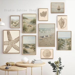 Op de afbeelding: Een verzameling ingelijste kustkunstprints in neutrale tinten, met afbeeldingen van schelpen, zeesterren, duinen en een zeilboot. De prints worden tentoongesteld op een witte muur boven twee ronde houten tafels.
