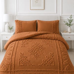 May include: A burnt orange bedding set featuring a comforter and two matching pillow shams. The fabric displays a raised, tufted texture with intricate botanical and geometric patterns, including a central sunburst motif and leaf borders.