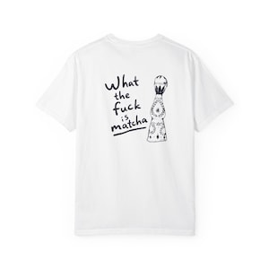Könnte beinhalten: Ein weißes T-Shirt mit kurzen Ärmeln und einem schwarzen Aufdruck auf der Rückseite. Die Grafik zeigt eine stilisierte Flasche mit komplexen Blumenmustern und dem handschriftlichen Text "What the fuck is matcha" links neben der Abbildung.
