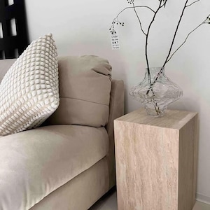 May include: A beige sofa with a textured pillow and a light-colored, square side table. A clear glass vase with branches sits on the table. The text "Under the tree 在树下 For you" is visible on the wall.