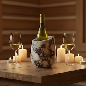 May include: A bottle of white wine in a marble wine chiller, with two wine glasses and several lit candles on a wooden table. The wine chiller has a white and gray marble pattern. The scene is set in a warm, inviting space.