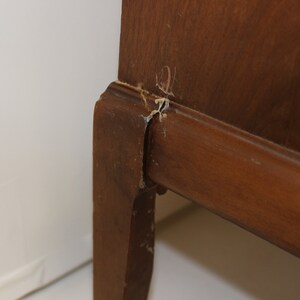 May include: Close-up of a wooden cabinet leg with a small crack and some wood chips missing.