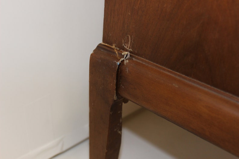 May include: Close-up of a wooden cabinet leg with a small crack and some wood chips missing.