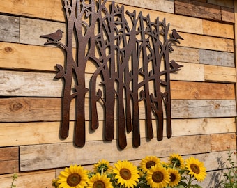 May include: A rectangular metal wall art piece featuring a laser-cut forest silhouette with bare tree trunks and branches. Three small bird figures are perched on the outer branches. The metal has a dark, textured, rusted brown finish.