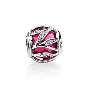 May include: A spherical silver charm bead featuring a vibrant, faceted magenta-pink stone center encased in a polished silver cage design. The silver overlay displays a leaf-like pattern accented with small, clear, sparkling inset stones.