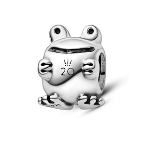 May include: A polished silver charm shaped like a stylized frog with large eyes and a wide mouth. The front features the engraved text 20 with a crown-like symbol above it. The foot is stamped with the hallmark 925, indicating sterling silver.
