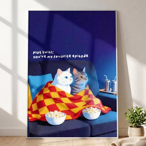 Puede incluir: Un cuadro enmarcado con dos gatos en un sofá azul, cubiertos por una manta roja y amarilla. La impresión incluye el texto "plot twist: you're my favorite episode". Dos cuencos de palomitas y bebidas están en una mesa auxiliar.