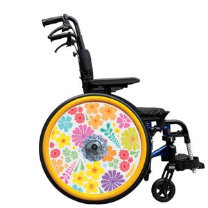 Könnte beinhalten: Blauer Rollstuhl mit schwarzem Sitz und Armlehnen. Die Räder haben einen gelben Rand und sind mit bunten Blumen in Rosa, Orange, Gelb und Blau verziert. Der Rollstuhl ist für Mobilität konzipiert.