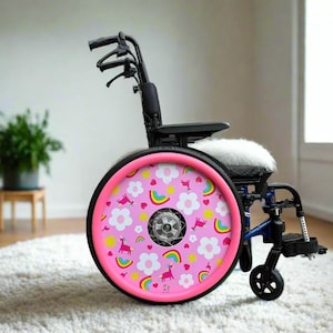 Op de afbeelding: Een zwarte en blauwe rolstoel met een roze wiel met een patroon van eenhoorns, regenbogen en bloemen. De zitting heeft een wit, pluizig kussen. De rolstoel staat op een wit tapijt.
