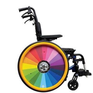 May include: A wheelchair featuring a rainbow wheel design. The wheel has a yellow rim and a spectrum of colours. The chair has a black seat and armrests, with a blue frame and black handles. The wheel diameter is approximately 60 cm.