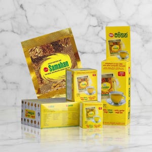 Puede incluir: Una variedad de productos de té de hierbas Samahan. La imagen muestra un sobre de papel dorado y varias cajas amarillas con el logotipo de Samahan y una taza de té. Los productos están dispuestos sobre una superficie de mármol blanco.