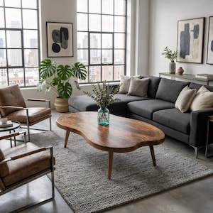 Op de afbeelding: Een niervormige salontafel gemaakt van natuurlijk hout met een glad, gepolijst oppervlak en drie taps toelopende poten. De tafel staat in het midden van een kamer en heeft een opvallend houtnerfpatroon en een laag ontwerp.