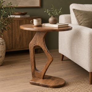 Puede incluir: Una mesa auxiliar de madera marrón con una superficie circular y una base de soporte única, curva y de marco abierto. La mesa presenta un acabado de veta de madera natural y un diseño de bordes redondeados, ofreciendo una superficie estable.