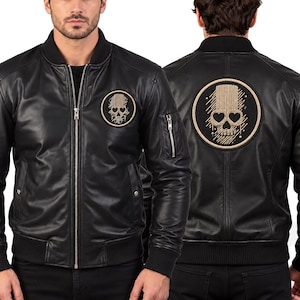 Puede incluir: Una chaqueta bomber de cuero negro con cuello, puños y dobladillo acanalados. La prenda cuenta con una cremallera frontal plateada, un bolsillo utilitario con cremallera en la manga izquierda y un parche circular en el pecho y la espalda.
