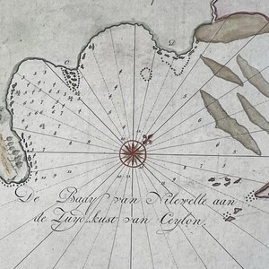 Puede incluir: Un mapa náutico antiguo de De Bady van Nilevelle aan de Zuyokust van Ceylon que presenta una rosa de los vientos central, líneas de rumbo radiantes, sondeos de profundidad y contornos costeros dibujados a mano con islas en tonos gris.