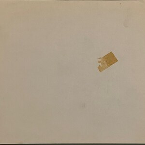 May include: A slightly off-white, rectangular sheet of paper with a small piece of torn, tan tape adhered to it. The paper has a few minor imperfections.