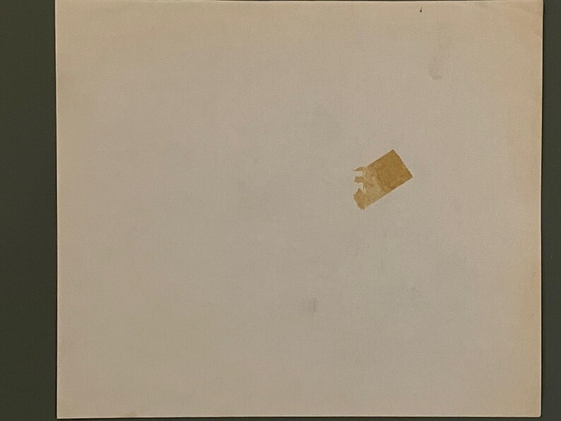 May include: A slightly off-white, rectangular sheet of paper with a small piece of torn, tan tape adhered to it. The paper has a few minor imperfections.