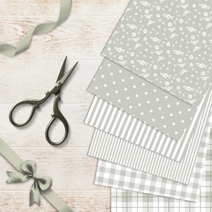 May include: A collection of patterned paper sheets in gray and white, featuring floral, polka dot, striped, and gingham designs. A pair of vintage scissors and a gray ribbon with a bow are also present, all arranged on a light wood surface.