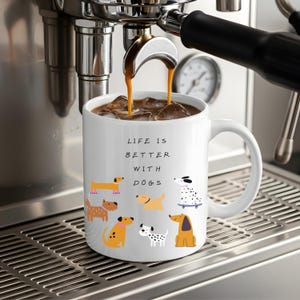 Könnte beinhalten: Ein weißer Keramikbecher gefüllt mit Eiskaffee, verziert mit dem schwarzen Text "LIFE IS BETTER WITH DOGS" und bunten Illustrationen verschiedener Hunderassen, darunter ein Dackel, ein Dalmatiner auf einem Skateboard und weitere gefleckte Hunde.