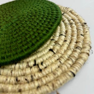 May include: A circular coaster featuring a vibrant green, tightly stitched fabric top layer layered over a larger, round base made of coiled, natural-colored fibrous material with dark brown flecks throughout the woven texture.