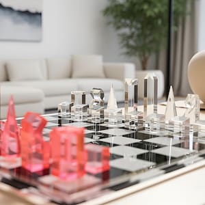 Peut inclure: Un jeu d'échecs moderne avec des pièces en acrylique transparent et rouge sur un échiquier. Les pièces sont des formes géométriques, dont des tours, des pyramides et des prismes rectangulaires. L'échiquier est posé sur une table en bois clair.