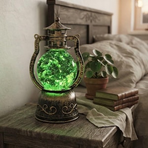 May include: A lantern-style lamp with a distressed bronze-coloured metal frame and a spherical glass centre that glows with a bright green light. The base features decorative scrollwork, and the top has a tiered, pagoda-inspired structure.