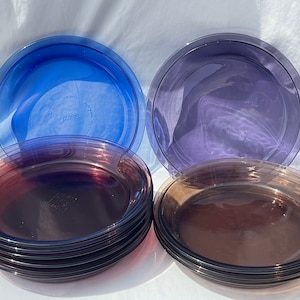 May include: A set of three glass pie plates in blue, purple, and brown. The plates are stacked on top of each other.