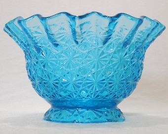 May include: A blue glass bowl with a ruffled rim and a starburst pattern. The bowl is made of clear glass with a blue tint.